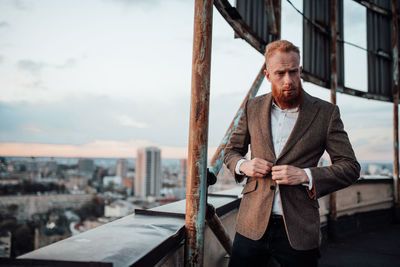 Portrait of young man standing in city against sky