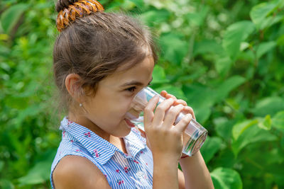 Side view of smiling girl drinking water from glass while looking away