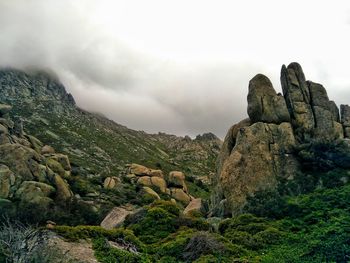 Scenic view of rocky mountains and rock formations with moss  against foggy sky