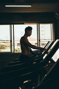 Side view of shirtless man standing by window