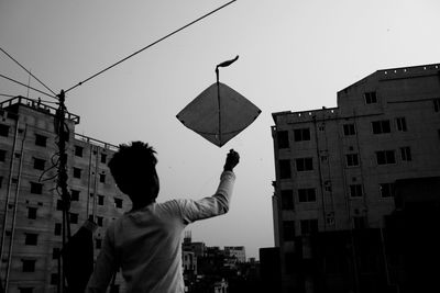 Rear view of man holding umbrella against buildings in city