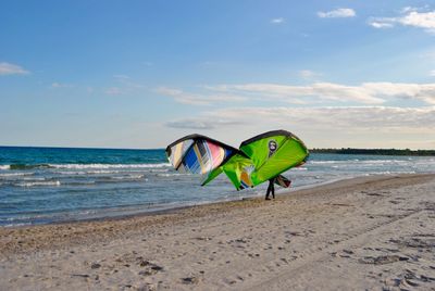 Low section of person with kiteboard walking on shore at beach against sky