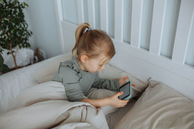 Young woman using mobile phone while lying on bed at home