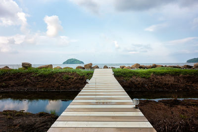 Boardwalk amidst plants on land against sky