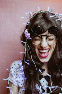 Close-up of smiling female model with illuminated string lights against peach backdrop