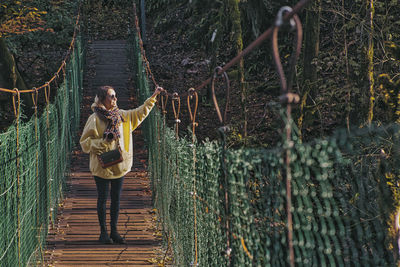 Woman standing on footbridge in forest