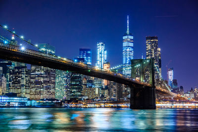 Illuminated buildings by river against sky in city at night