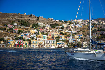 Sailboats moored on sea by buildings in city against sky