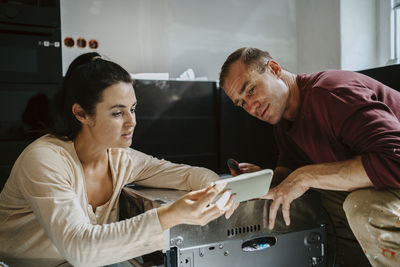 Man and woman discussing over smart phone while renovating kitchen at home