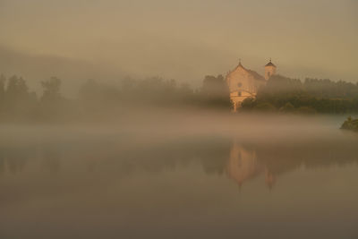 Reflection of building in lake against sky during foggy weather