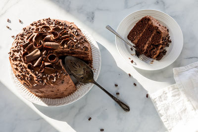 A chocolate cake decorated with chocolate curls, sitting in bright sunlight.