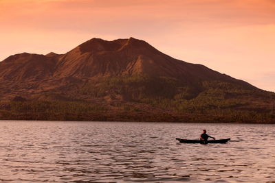 Man in boat on lake against mount batur
