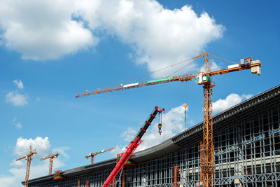 Low angle view of cranes at construction site against sky