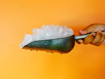 Close-up of hand holding ice cream against orange background