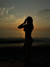 Silhouette woman standing at beach against sky during sunset