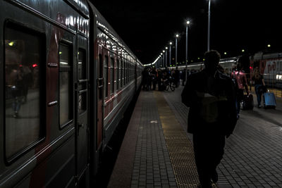 Rear view of man walking by train at railroad station during night