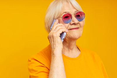 Young woman wearing sunglasses against yellow background