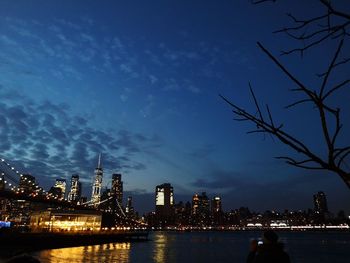 Illuminated buildings by river against sky at night