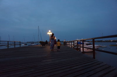 People walking on pier at sea against clear sky