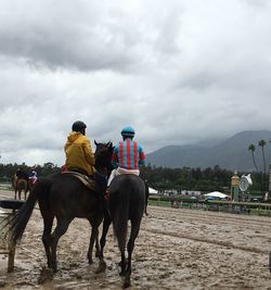 People riding horses on sand against sky