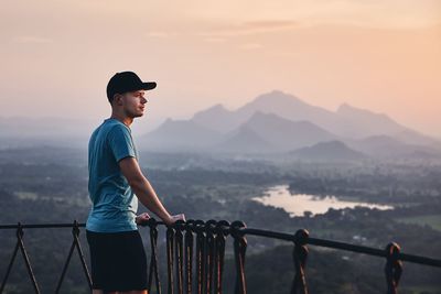 Side view of mid adult man looking at landscape while standing on mountain against sky during sunset