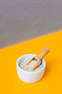 Wooden spoon with sesame seeds lies in a white mortar on a yellow background. healthy eating. keto