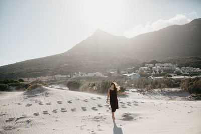 Full length of young woman walking at beach against mountain