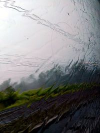 Close-up of wet glass window against lake