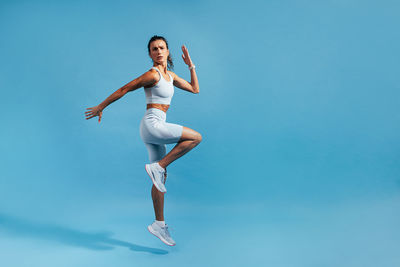 Full length of woman exercising against blue background