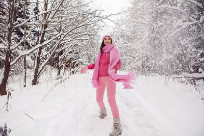 Woman standing on a path in the woods in pink clothes a jacket a knitted scarf forest in winter
