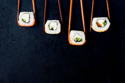 Fresh tasty sushi with salmon in wooden chopsticks on a dark background. 