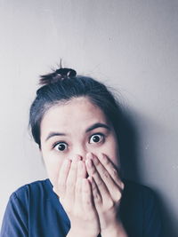 Portrait of surprised young woman hands covering mouth against wall