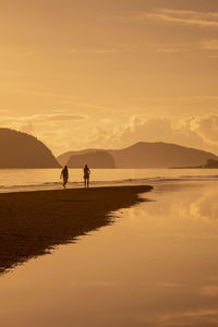 Silhouette people at beach against sky during sunset