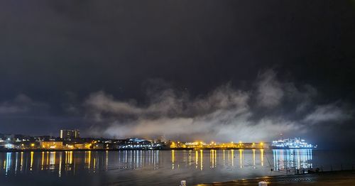 Illuminated city by river against sky at night