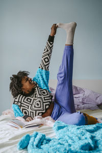 Happy young woman touching toes while lying in bedroom