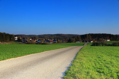 Road amidst field against clear blue sky