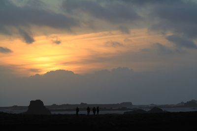 Silhouette people on rocks against sky during sunset