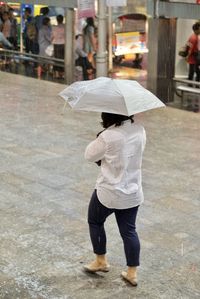 Rear view of woman walking with umbrella on footpath during rainy season