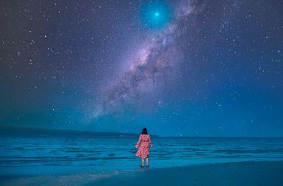 Rear view of woman standing at beach against sky at night