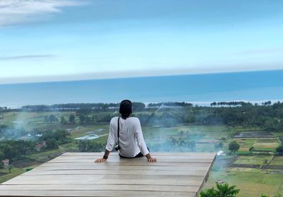 Rear view of man sitting on observation point against sky