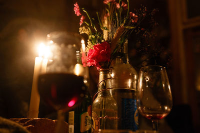 Wineglass and flower vase by lit candles on table