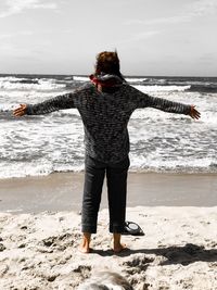 Rear view of woman with arms outstretched standing on beach 