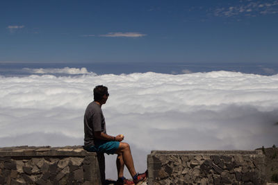 Man sitting on mountain watching the sea of clouds below him
