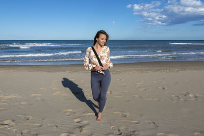 Young caucasian woman walking alone on the sandy beach at sunset