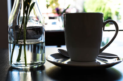 Close-up of coffee cup by glass vase on table