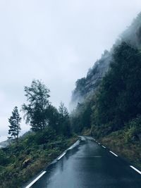 Empty road amidst trees against sky during rainy season