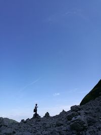 Low angle view of man standing on rock against blue sky