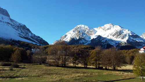 Scenic view of snow covered mountains against clear blue sky