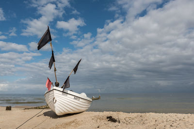 Boat moored on sea shore against cloudy sky