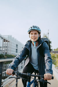 Smiling female delivery person wearing helmet and sitting on bicycle